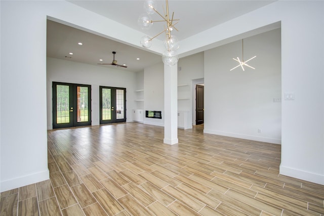 unfurnished living room featuring french doors, ceiling fan with notable chandelier, a multi sided fireplace, light hardwood / wood-style flooring, and a towering ceiling