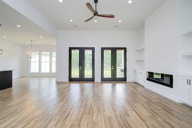 unfurnished living room featuring ceiling fan with notable chandelier, light wood-type flooring, a high ceiling, and french doors