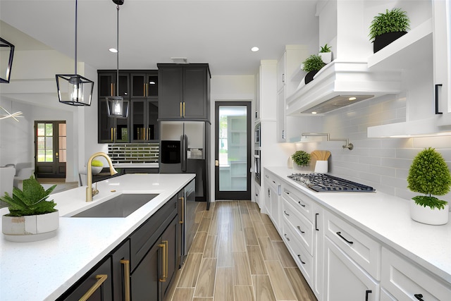 kitchen with light stone countertops, white cabinetry, sink, hanging light fixtures, and backsplash