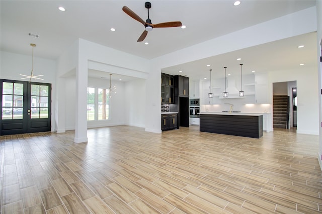 unfurnished living room with ceiling fan with notable chandelier, french doors, sink, and light hardwood / wood-style flooring