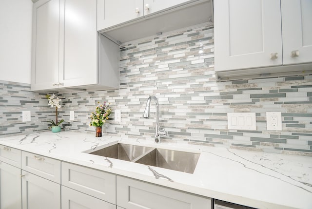 kitchen with decorative backsplash, white cabinets, light stone countertops, and sink