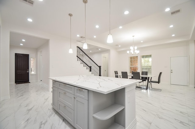 kitchen featuring gray cabinetry, an inviting chandelier, decorative light fixtures, a kitchen island, and light stone counters