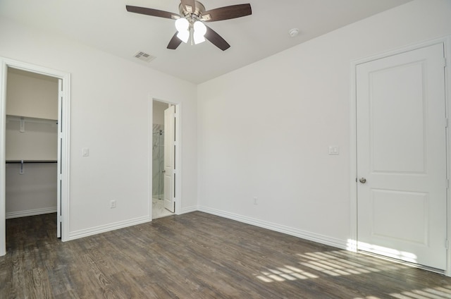 unfurnished bedroom with a walk in closet, ensuite bath, ceiling fan, dark wood-type flooring, and a closet