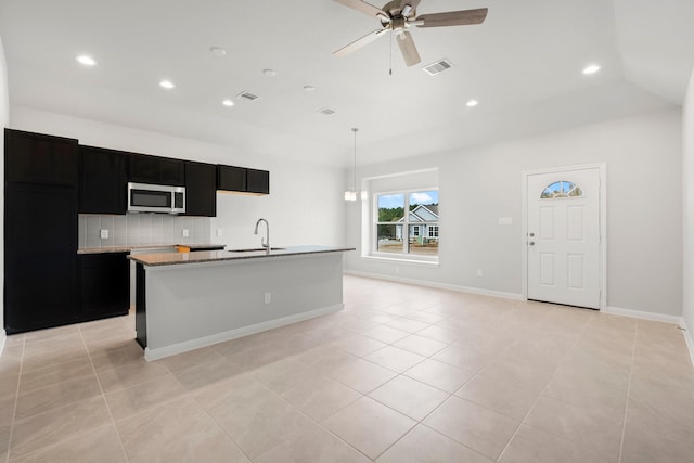 kitchen with decorative backsplash, ceiling fan with notable chandelier, sink, pendant lighting, and an island with sink