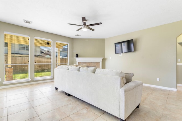 tiled living room with a tiled fireplace, ceiling fan, and plenty of natural light