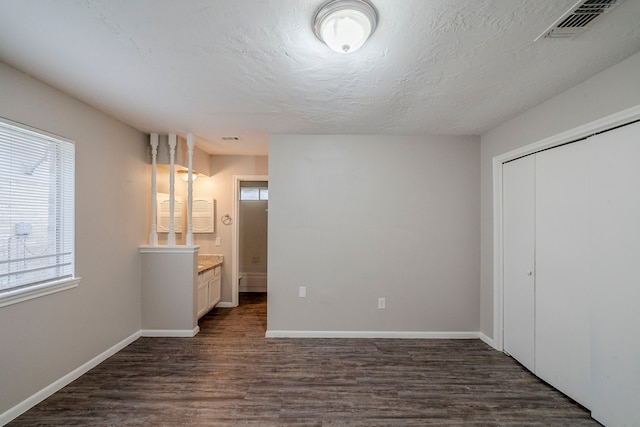 unfurnished bedroom featuring a closet, dark hardwood / wood-style flooring, a textured ceiling, and ensuite bath