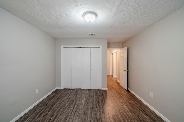 unfurnished bedroom featuring a textured ceiling, dark hardwood / wood-style floors, and a closet