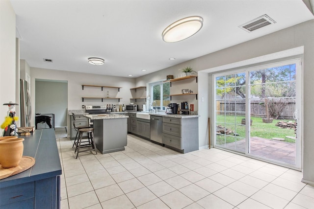 kitchen featuring appliances with stainless steel finishes, light tile patterned floors, a center island, gray cabinets, and a breakfast bar area