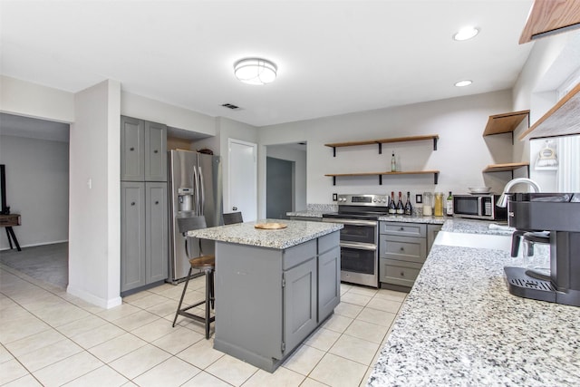 kitchen featuring gray cabinetry, a kitchen island, light stone counters, and appliances with stainless steel finishes