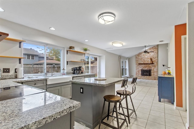 kitchen with light stone countertops, sink, a brick fireplace, gray cabinets, and a kitchen island