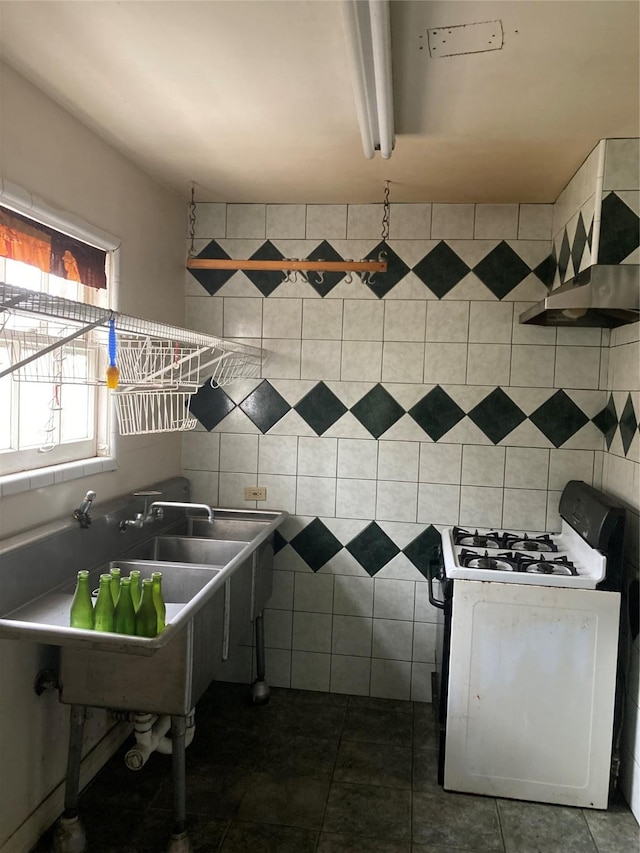 kitchen with dark tile patterned floors, white gas range, and tile walls