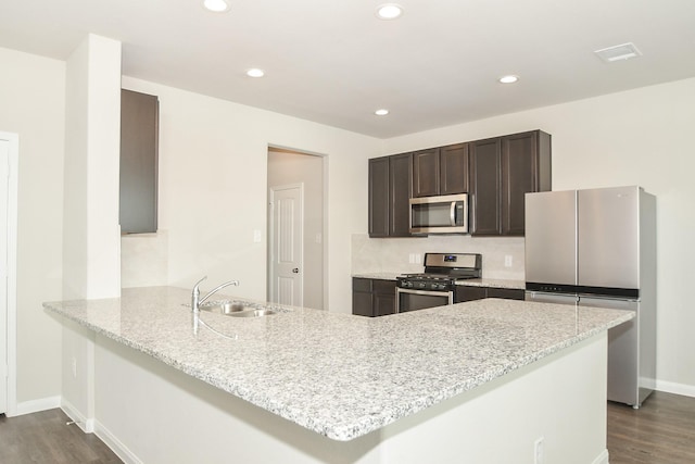 kitchen featuring sink, stainless steel appliances, light stone counters, dark hardwood / wood-style flooring, and kitchen peninsula