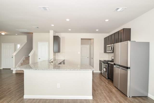 kitchen with kitchen peninsula, light stone counters, stainless steel appliances, sink, and light hardwood / wood-style flooring