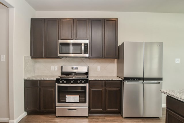 kitchen with dark brown cabinetry, appliances with stainless steel finishes, tasteful backsplash, light stone counters, and wood-type flooring