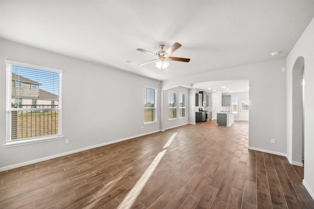 unfurnished living room featuring ceiling fan, a healthy amount of sunlight, and dark wood-type flooring