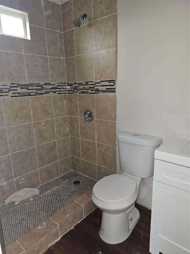 bathroom featuring toilet, hardwood / wood-style floors, vanity, and a tile shower