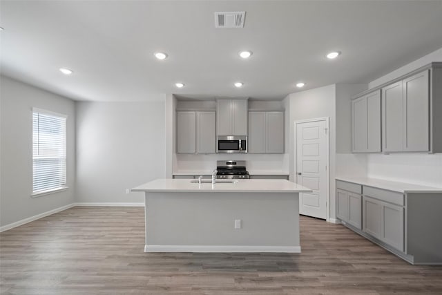 kitchen with stainless steel appliances, gray cabinets, a kitchen island with sink, and light hardwood / wood-style floors