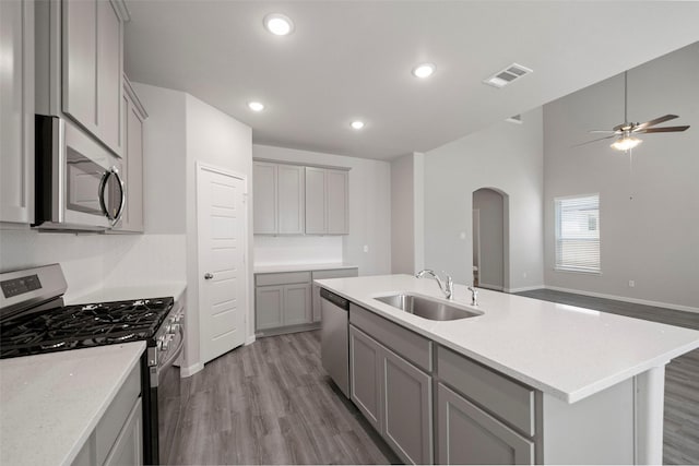 kitchen with a center island with sink, sink, gray cabinets, wood-type flooring, and stainless steel appliances