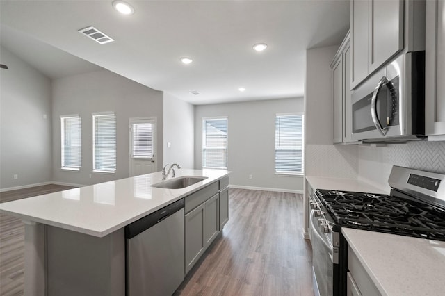 kitchen with sink, gray cabinets, a kitchen island with sink, appliances with stainless steel finishes, and hardwood / wood-style flooring