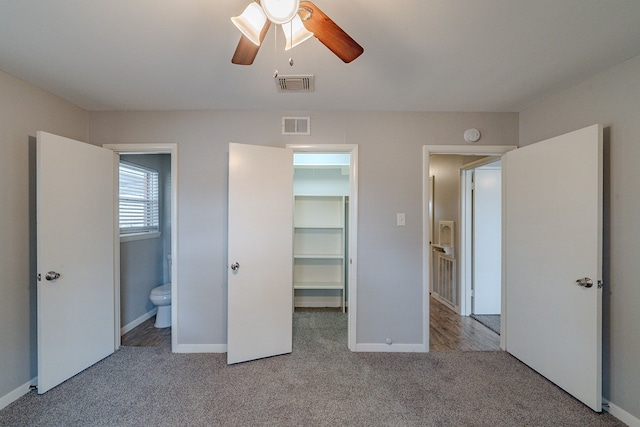 unfurnished bedroom with ensuite bathroom, ceiling fan, a spacious closet, light colored carpet, and a closet