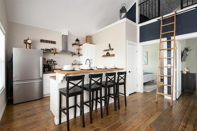 kitchen featuring a kitchen breakfast bar, stainless steel refrigerator, white cabinetry, and wall chimney exhaust hood