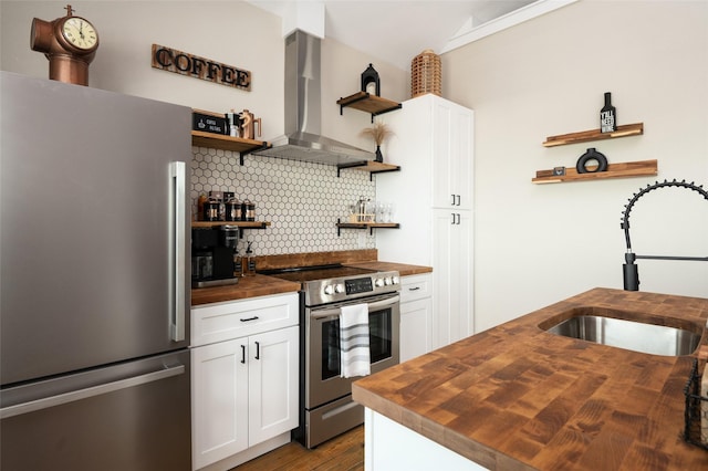 kitchen with sink, wall chimney range hood, butcher block countertops, white cabinets, and appliances with stainless steel finishes