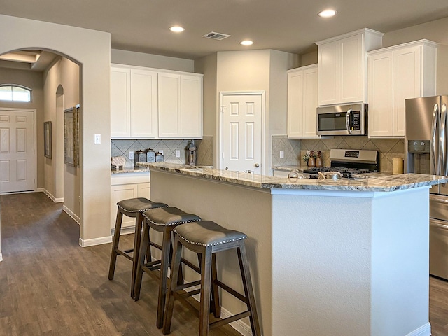 kitchen featuring a kitchen island with sink, white cabinets, light stone countertops, appliances with stainless steel finishes, and dark hardwood / wood-style flooring