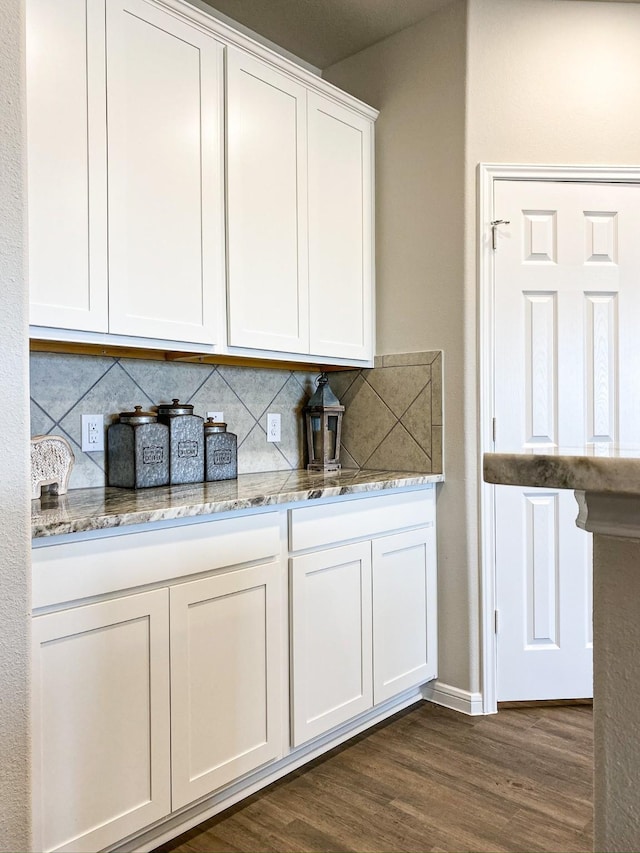 kitchen with white cabinets, dark hardwood / wood-style floors, light stone countertops, and tasteful backsplash