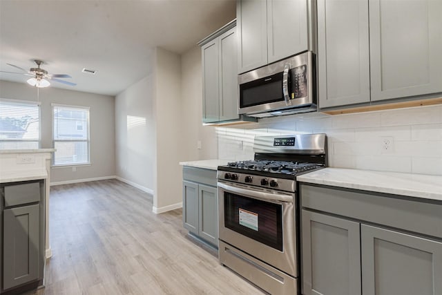 kitchen with light stone countertops, tasteful backsplash, gray cabinetry, stainless steel appliances, and light hardwood / wood-style flooring