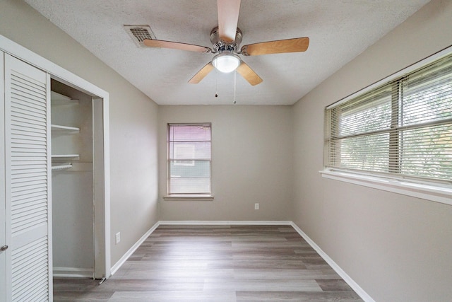 unfurnished bedroom with a closet, ceiling fan, hardwood / wood-style floors, and a textured ceiling