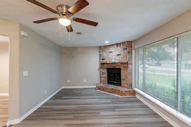 unfurnished living room with a fireplace, wood-type flooring, a wealth of natural light, and ceiling fan