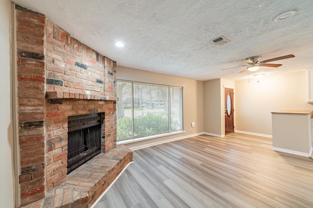 unfurnished living room with a fireplace, a textured ceiling, light hardwood / wood-style flooring, and ceiling fan