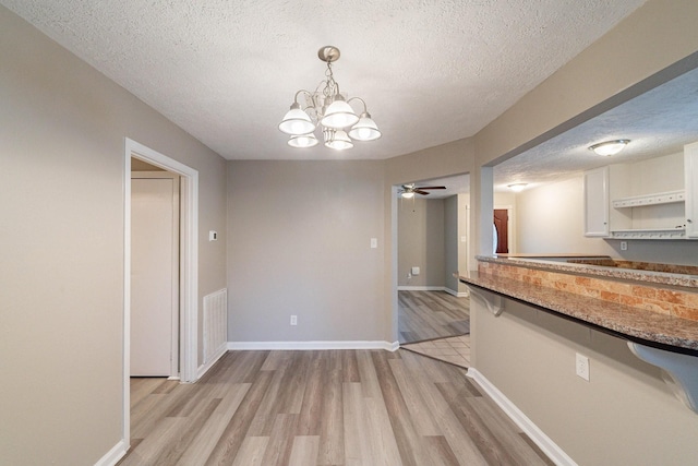 unfurnished dining area with ceiling fan with notable chandelier, a textured ceiling, and light hardwood / wood-style flooring