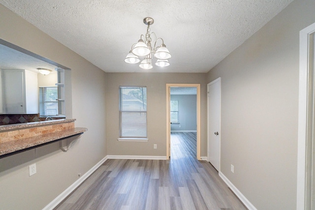 unfurnished dining area featuring a chandelier, a textured ceiling, hardwood / wood-style flooring, and a healthy amount of sunlight