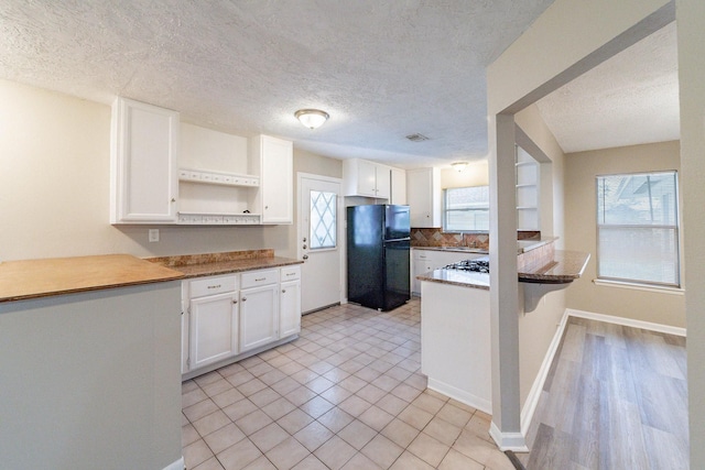 kitchen with kitchen peninsula, a wealth of natural light, black refrigerator, and white cabinets