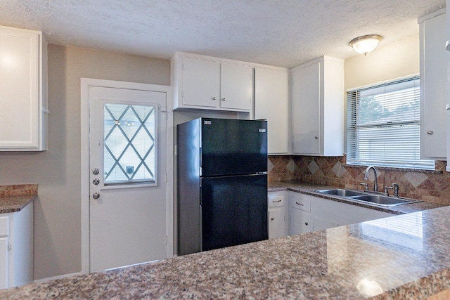 kitchen featuring white cabinets, black refrigerator, sink, a textured ceiling, and tasteful backsplash