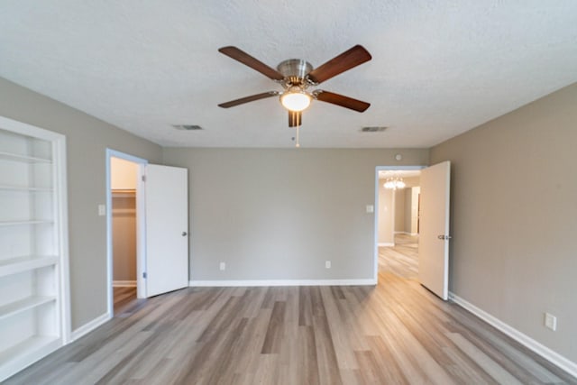 unfurnished bedroom featuring a spacious closet, a textured ceiling, a closet, ceiling fan with notable chandelier, and light wood-type flooring