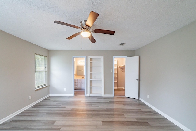 unfurnished bedroom featuring light wood-type flooring, ensuite bath, ceiling fan, a spacious closet, and a closet