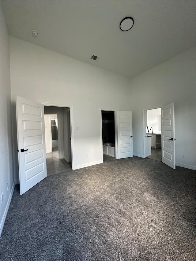 unfurnished bedroom with dark colored carpet, a high ceiling, and connected bathroom