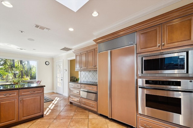 kitchen with dark stone counters, built in appliances, decorative backsplash, light tile patterned floors, and ornamental molding