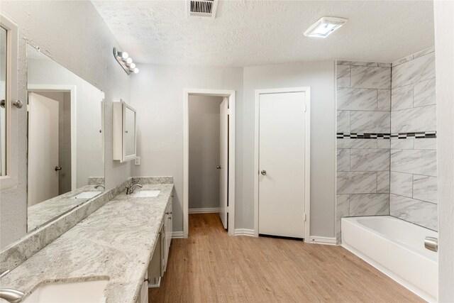 bathroom with hardwood / wood-style floors, vanity, a textured ceiling, and tiled shower / bath