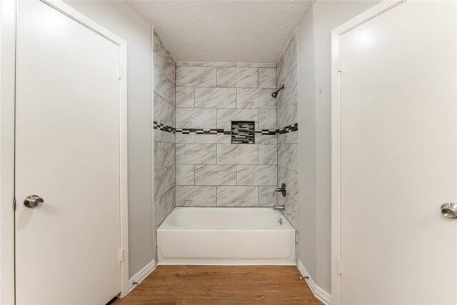 bathroom with a textured ceiling, hardwood / wood-style flooring, and tiled shower / bath