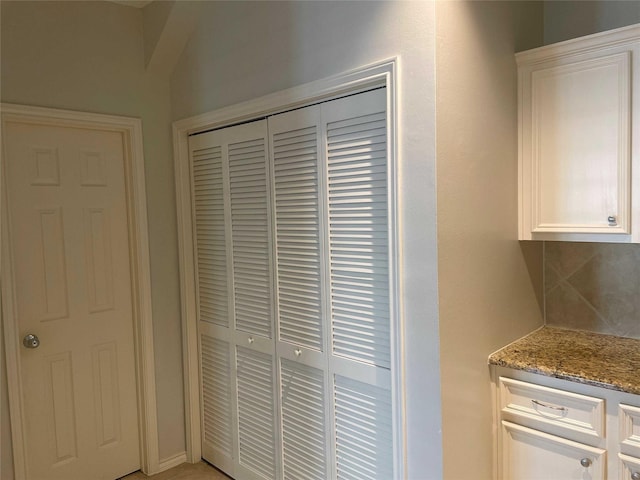 interior space featuring decorative backsplash, white cabinetry, and light stone counters