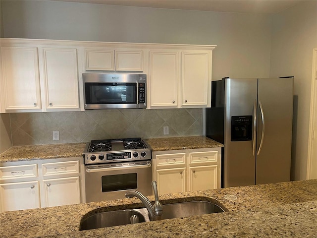 kitchen with white cabinets, appliances with stainless steel finishes, light stone counters, and sink