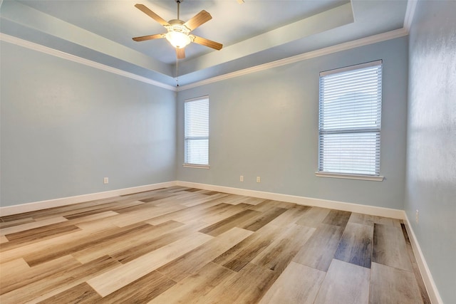 empty room featuring a raised ceiling, baseboards, crown molding, and light wood finished floors