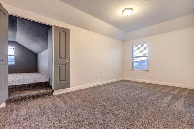 carpeted empty room with vaulted ceiling, a textured ceiling, and baseboards