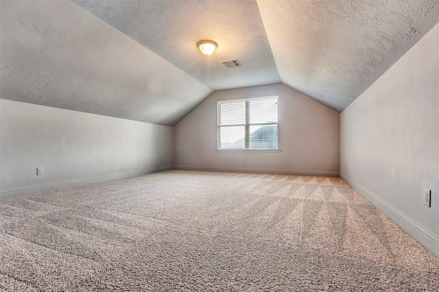 additional living space featuring visible vents, light carpet, vaulted ceiling, a textured ceiling, and baseboards