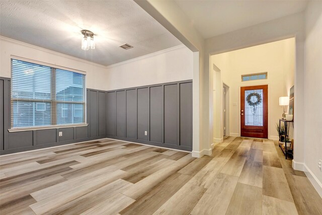 foyer entrance featuring ornamental molding, light wood-type flooring, visible vents, and a decorative wall