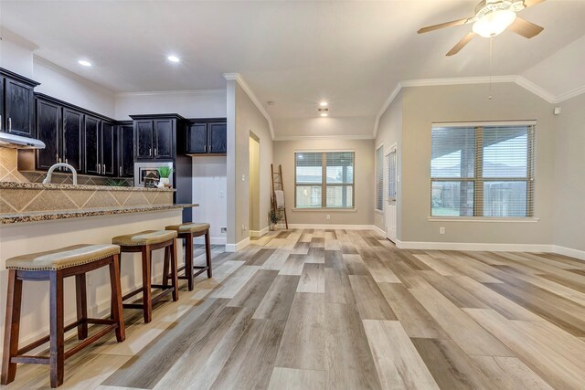 kitchen featuring a breakfast bar area, light wood-style flooring, dark cabinetry, backsplash, and light stone countertops