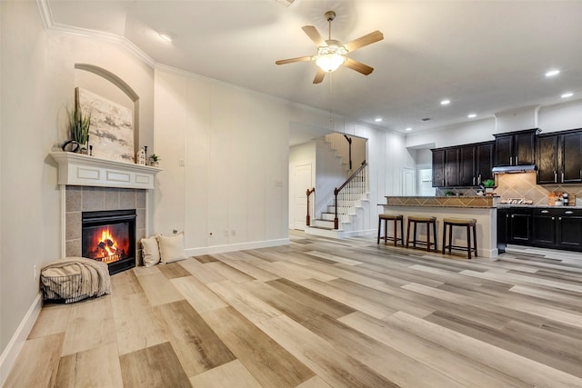 living area featuring light wood-type flooring, a fireplace, stairway, and baseboards